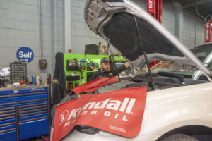 Hybrid vehicle service warning sign in an auto repair shop, highlighting high-voltage electricity safety precautions for EV and hybrid repairs.