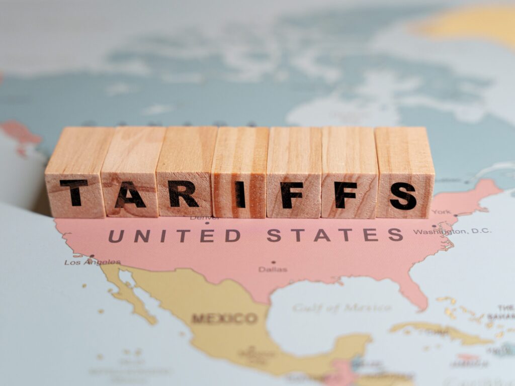 Wooden blocks spelling TARIFFS are placed on a map of North America, specifically over the United States and Mexico