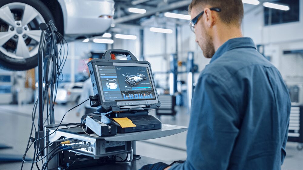 Automotive technician using advanced diagnostic calibration software on a rugged laptop in a modern vehicle repair shop. Car diagnostics, ADAS calibration, and digital vehicle inspection in an auto service center.