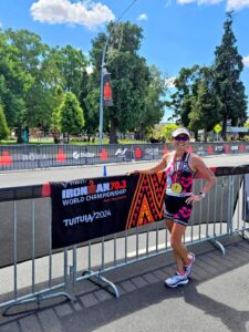 Victoria Repice smiling after completing the Ironman 70.3 World Championship 2024 in Taupō, New Zealand, wearing her race gear and medal while standing by the event signage.