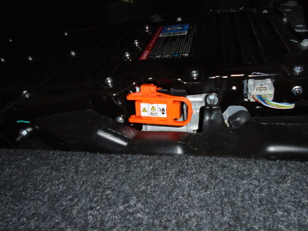 High-voltage service disconnect plug located behind the left rear seat on a Ford Fusion hybrid, used for safely disabling the HV battery.