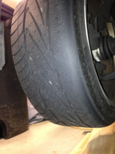 Close-up of a car tire with severe tread wear, showing bald spots and uneven surface indicating need for replacement.