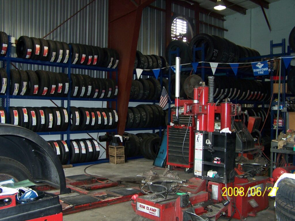Automotive tire shop with rows of new tires on shelves and red tire mounting equipment in the service area.