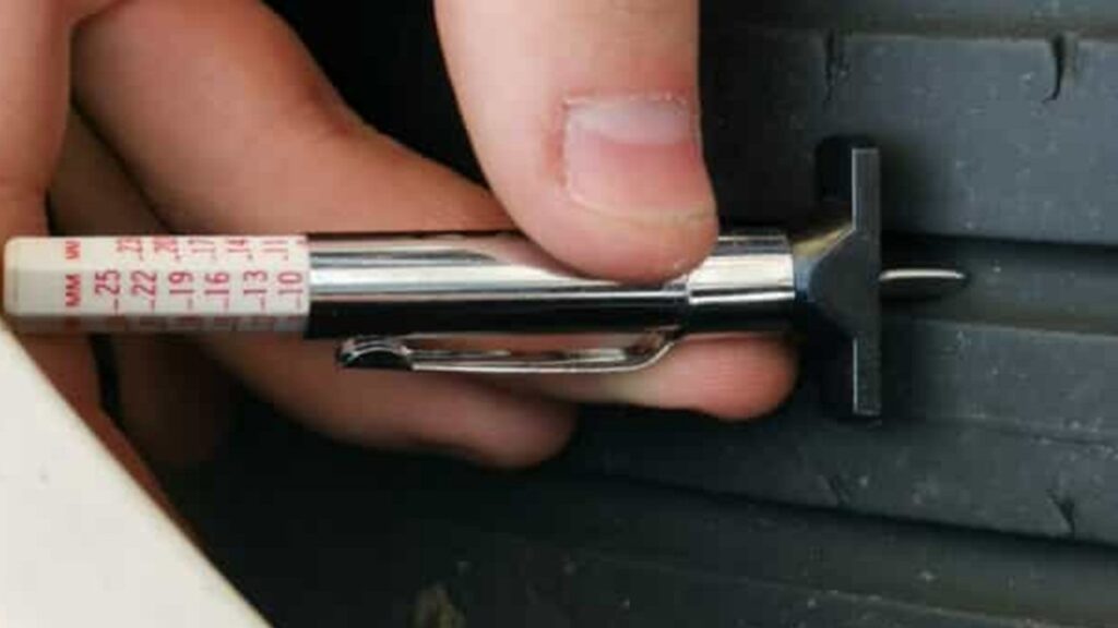 Close-up of a tread depth gauge measuring tire tread wear to check safety and replacement needs.