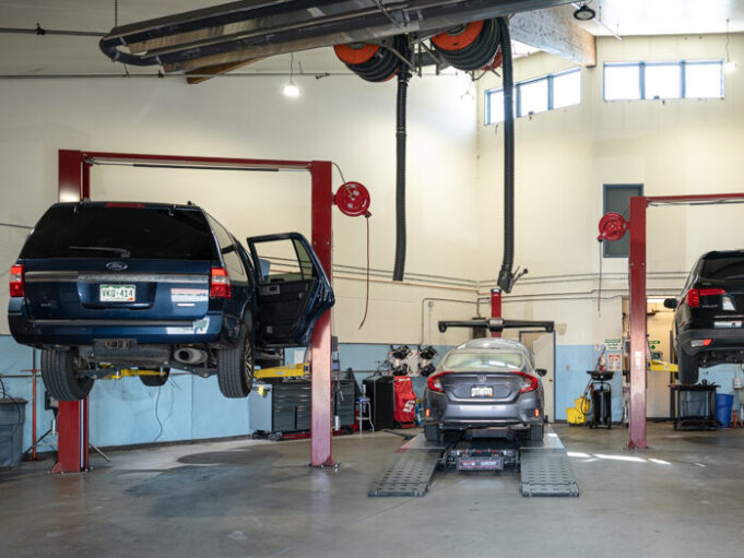 Three service bays inside the Autovisions repair facility, with two vehicles on lifts and one centered on the ground. The shop is clean, well-lit, and actively in use.