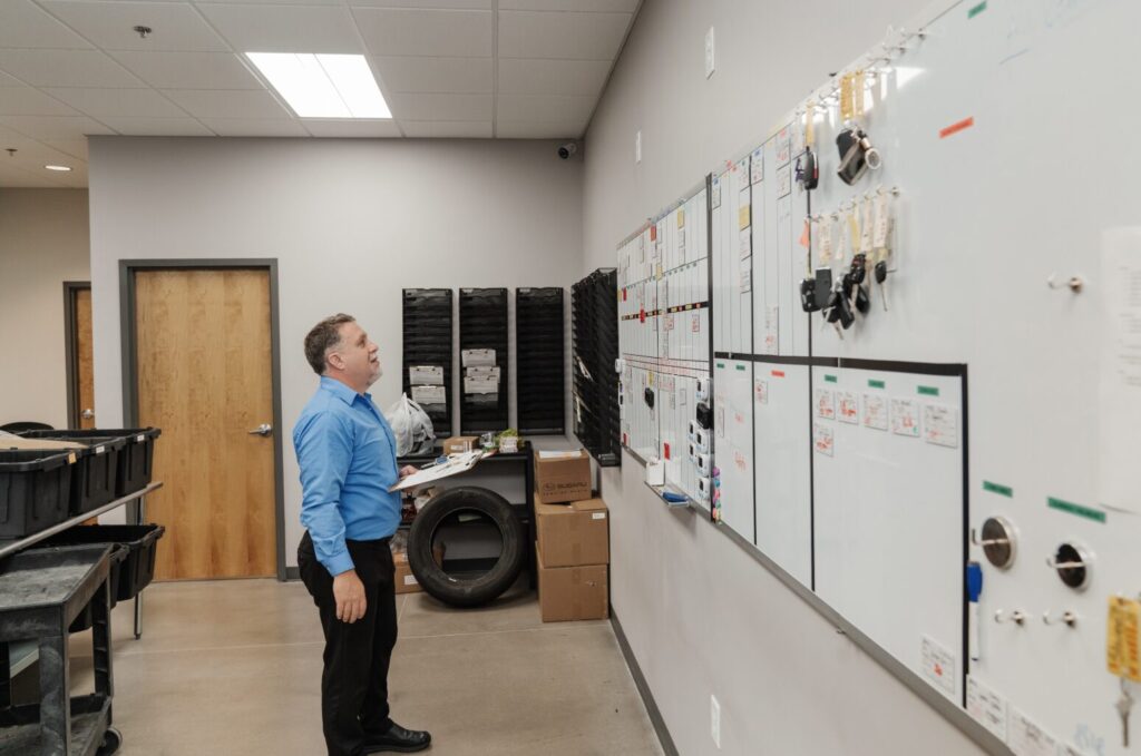 Automotive shop manager reviewing workflow board with service schedules and car keys at Getz Automotive.