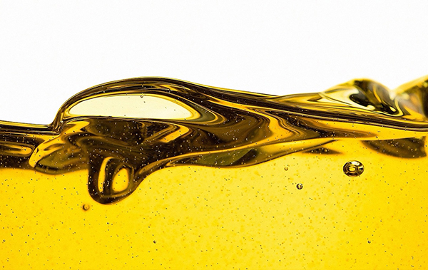 Close-up of golden motor oil flowing with bubbles on a white background, illustrating engine lubrication and viscosity.