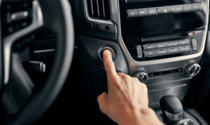 Driver pressing push-button start in a modern car, illustrating stop-start ignition technology for fuel efficiency and convenience.